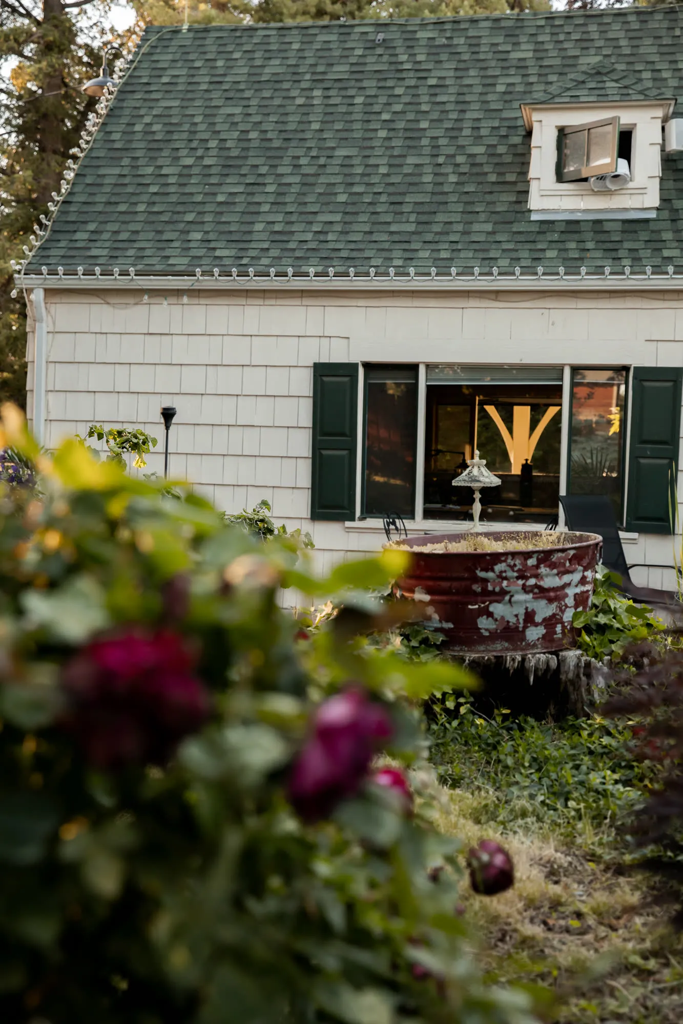 Cream shingles, green shutters, and a weathered metal planter