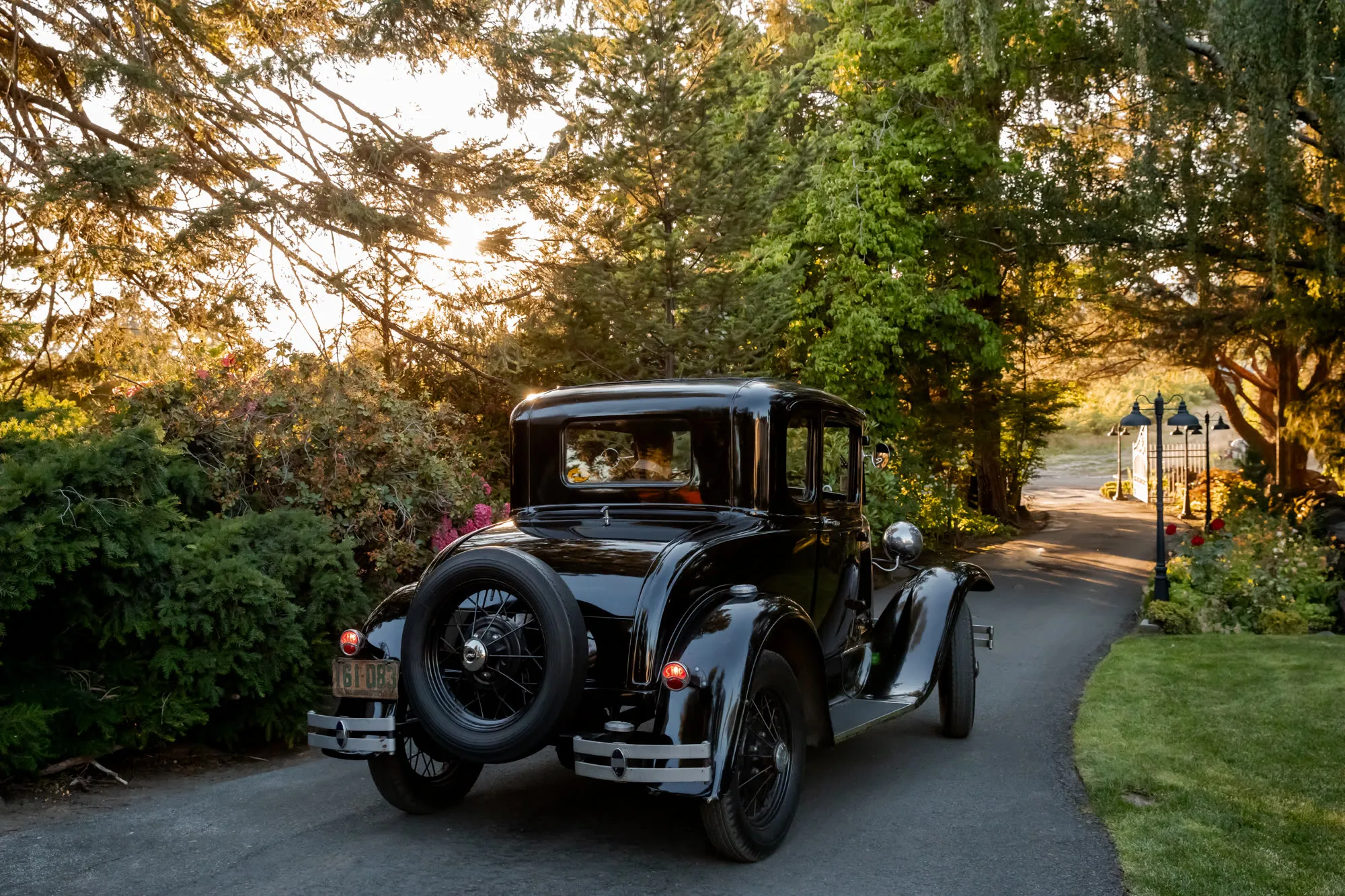 Model A on the drive at sunset, people small in the cabin