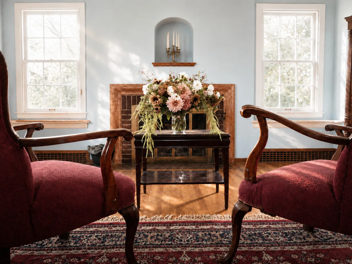 Parlor with burgundy chairs, flowers, and the brick fireplace
